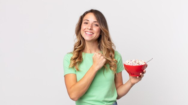 Pretty thin woman feeling happy and facing a challenge or\
celebrating and holding a breakfast bowl