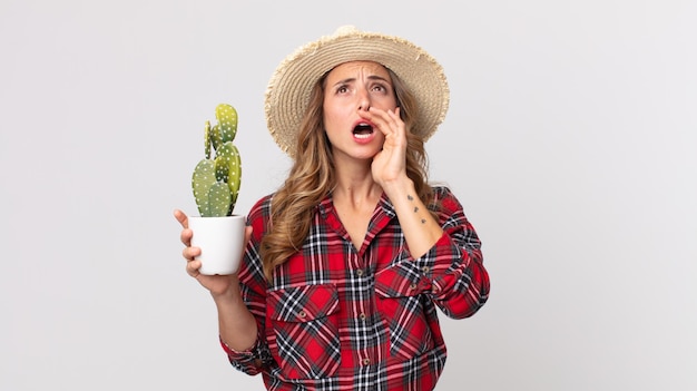 Donna abbastanza magra che si sente felice, fa un grande grido con le mani vicino alla bocca che tiene un cactus. concetto di contadino