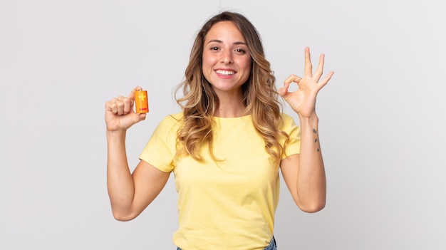 Pretty thin woman feeling happy, showing approval with okay gesture and holding batteries