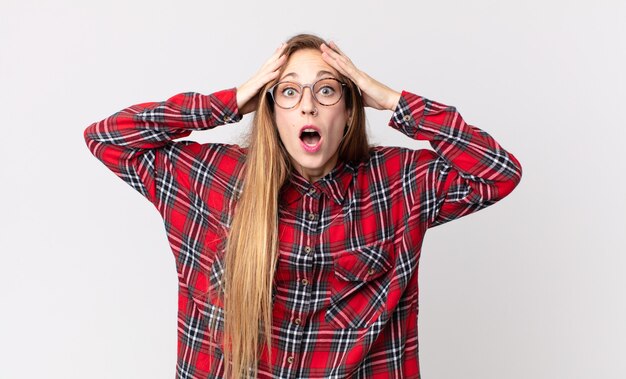 Pretty thin woman feeling horrified and shocked, raising hands to head and panicking at a mistake