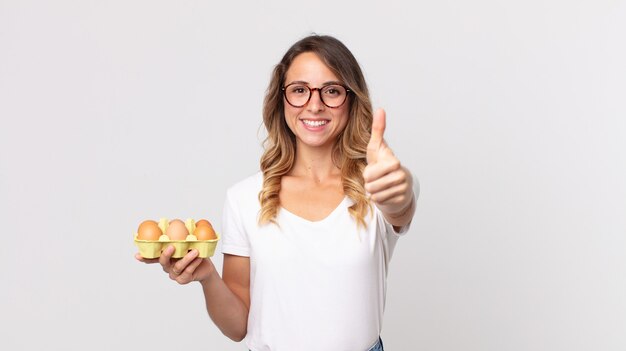 Pretty thin woman feeling proud,smiling positively with thumbs up and holding an eggs box