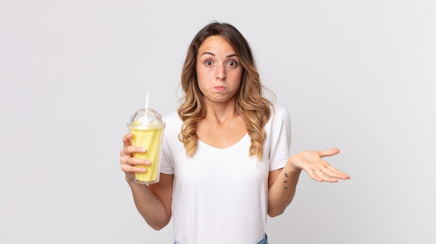 Довольно худая женщина чувствует себя озадаченной и смущенной, сомневается и держит ванильный молочный коктейль