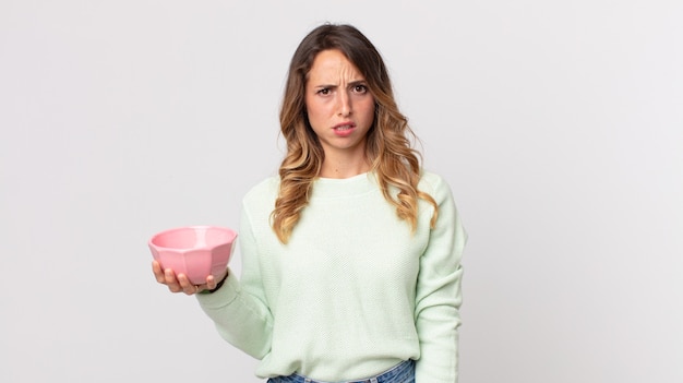 Pretty thin woman feeling puzzled and confused and holding an empty pot bowl