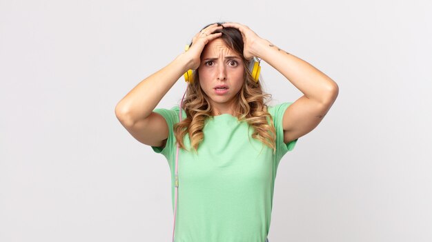 Foto donna abbastanza magra che si sente stressata, ansiosa o spaventata, con le mani sulla testa che ascolta musica con le cuffie