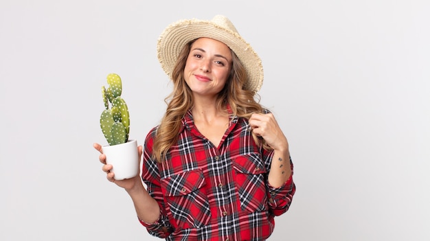 Photo pretty thin woman looking arrogant, successful, positive and proud holding a cactus. farmer concept
