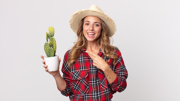 Foto donna abbastanza magra che sembra eccitata e sorpresa che indica il lato che tiene un cactus. concetto di contadino