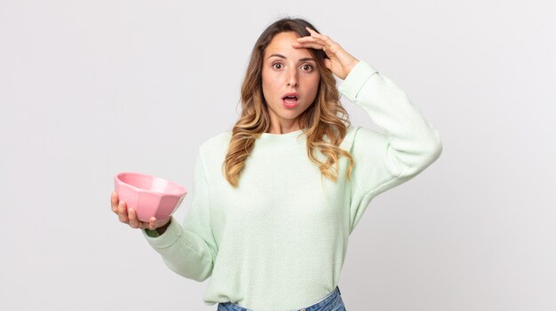 Pretty thin woman looking happy, astonished and surprised and holding an empty pot bowl