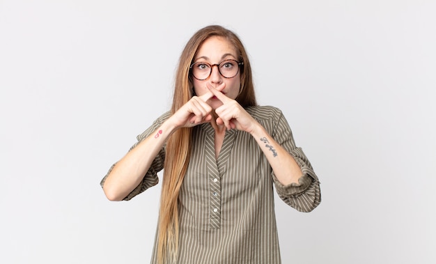 Pretty thin woman looking serious and displeased with both fingers crossed up front in rejection, asking for silence