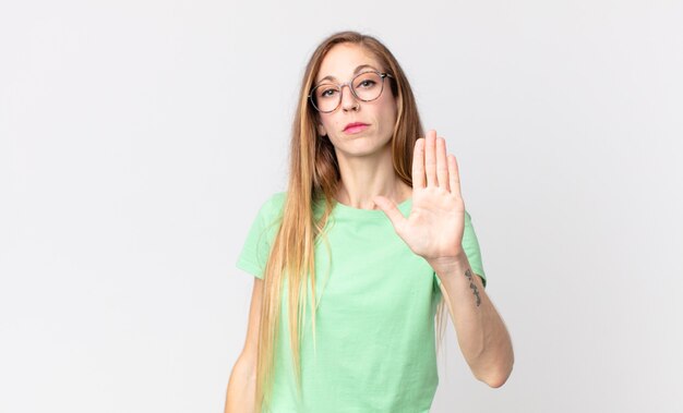 Pretty thin woman looking serious, stern, displeased and angry showing open palm making stop gesture