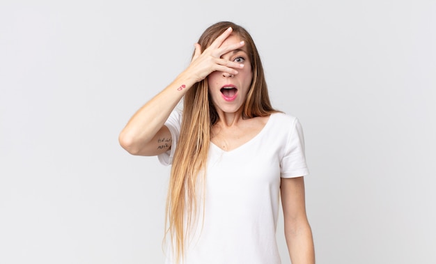 Pretty thin woman looking shocked, scared or terrified, covering face with hand and peeking between fingers