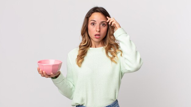 Pretty thin woman looking surprised, realizing a new thought, idea or concept and holding an empty pot bowl