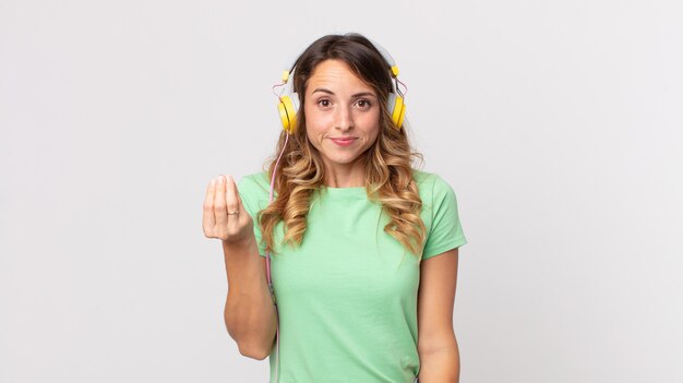 Pretty thin woman making capice or money gesture, telling you to pay listening music with headphones