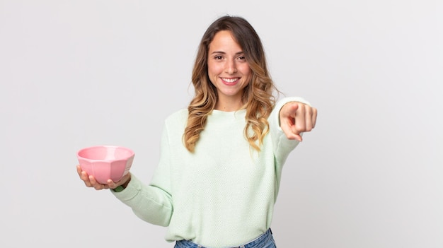 Pretty thin woman pointing at camera choosing you and holding an empty pot bowl