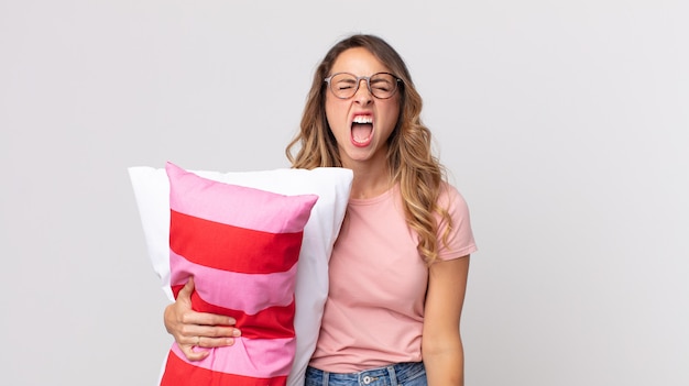 Pretty thin woman shouting aggressively, looking very angry wearing pajamas and holding a pillow