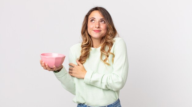 Pretty thin woman shrugging, feeling confused and uncertain and holding an empty pot bowl