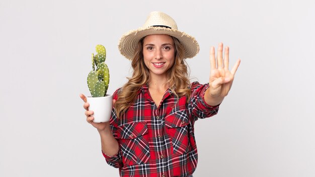 Pretty thin woman smiling and looking friendly, showing number four holding a cactus. farmer concept