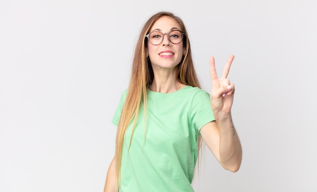 Pretty thin woman smiling and looking happy, carefree and positive, gesturing victory or peace with one hand