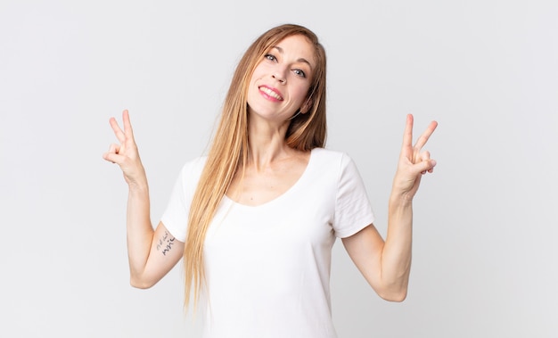 Pretty thin woman smiling and looking happy, friendly and satisfied, gesturing victory or peace with both hands