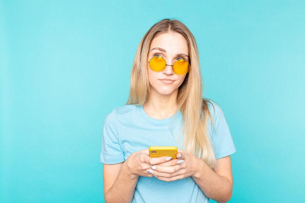 pretty thinking young woman posing isolated on blue wall using mobile phone.