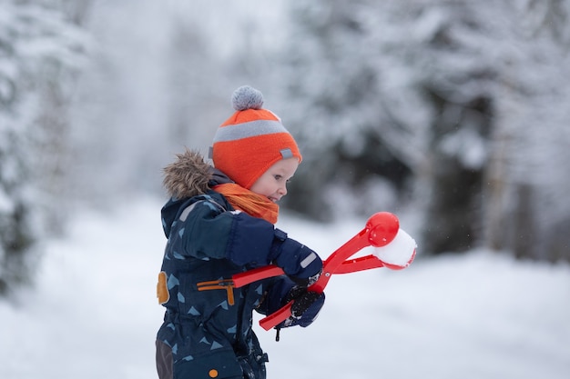 Симпатичная девочка малыша в зимней одежде весело на улице в снежный день. Девушка лепит снежки. Копировать пространство