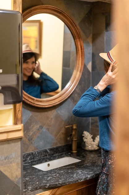 A pretty tourist in a hotel bathroom putting on her hat before going out to visit the city on vacation