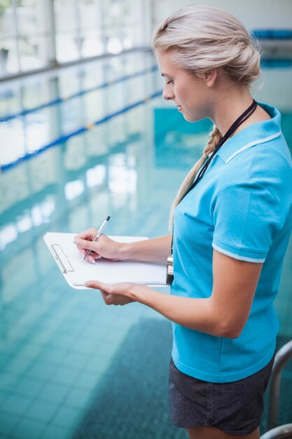 Pretty trainer writing on clipboard at the pool