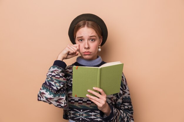 Photo pretty unhappy woman in earrings holding diary and crying isolated over beige wall