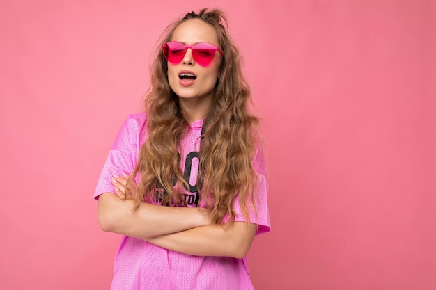 Abbastanza sconvolto chiedendo giovane donna bionda riccia isolata sopra la parete di fondo rosa che indossa rosa casual