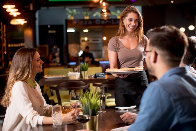 Pretty waiter woman serving group of friends with food in the restaurant