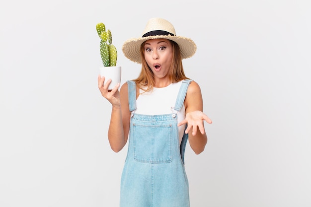 Pretty woman amazed, shocked and astonished with an unbelievable surprise and holding a cactus decorative plant