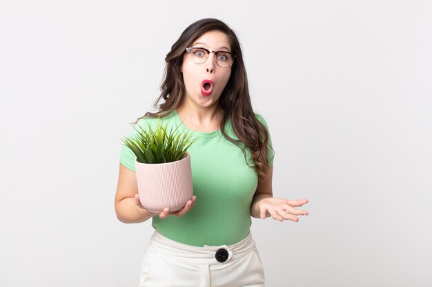 Pretty woman amazed, shocked and astonished with an unbelievable surprise and holding a decorative plant