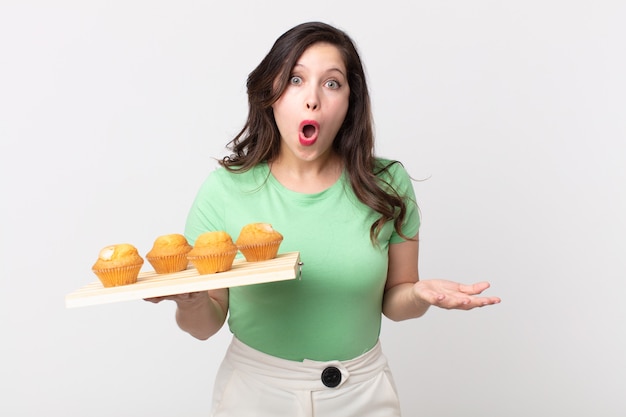 Pretty woman amazed, shocked and astonished with an unbelievable surprise and holding a muffins tray