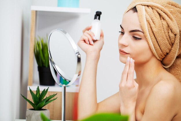 Pretty woman applying makeup on face at home.