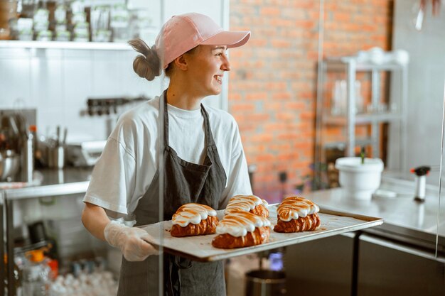 写真 きれいな女性のパン屋は店で焦げたアルブミンクリームと美しいクロワッサンを保持します