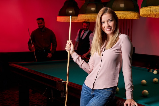 Pretty woman in the bar next to billiards table pool, people\
playing snooker