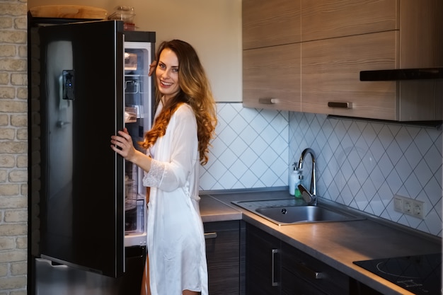 Pretty woman in bathrobe taking out the food from fridge in the morning