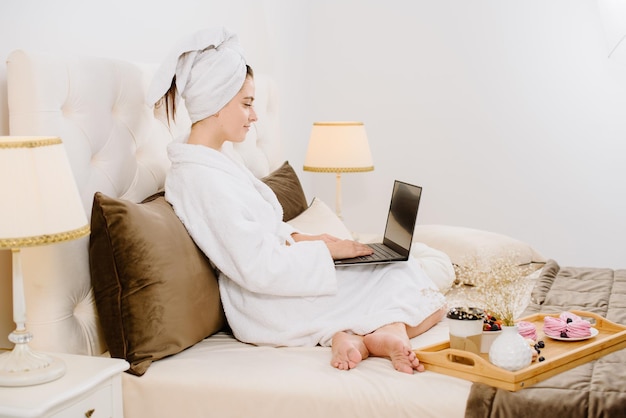 Pretty woman in bathrobe and towel on the head using a laptop on the bed at home