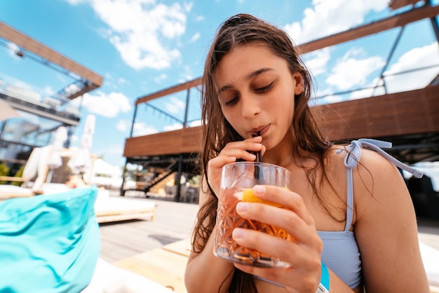 Pretty woman in bikini drinking cocktail at pool party