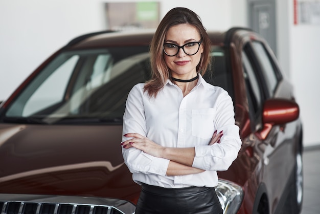 自動車サロンで真新しい車の近くでポーズをとって黒いスカートのきれいな女性