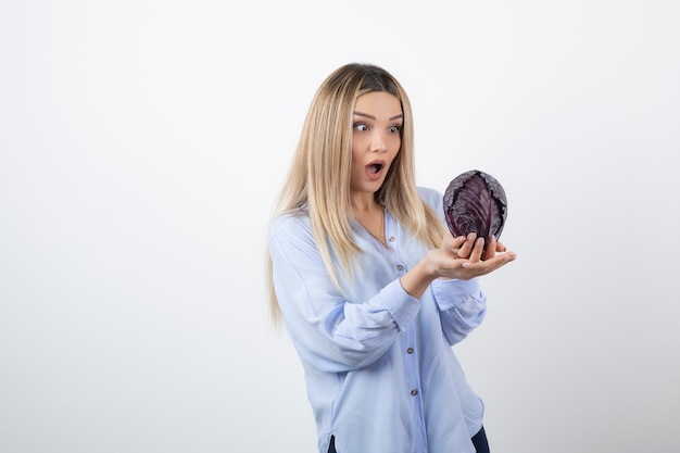 Pretty woman in blue outfit looking at purple cabbage on white.