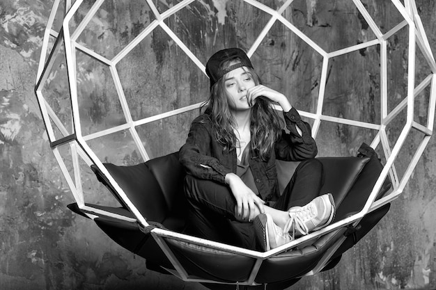 Pretty woman in cap sitting in geometric chair