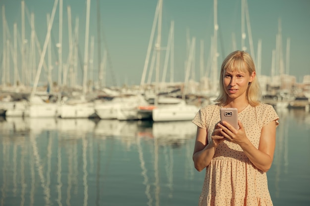 A pretty woman communicates on a smartphone against the background of a marina and yachts