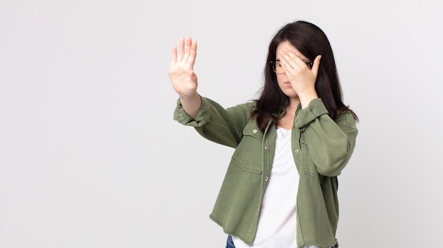 Bella donna che copre il viso con la mano e mette l'altra mano davanti per fermare la fotocamera, rifiutando foto o immagini