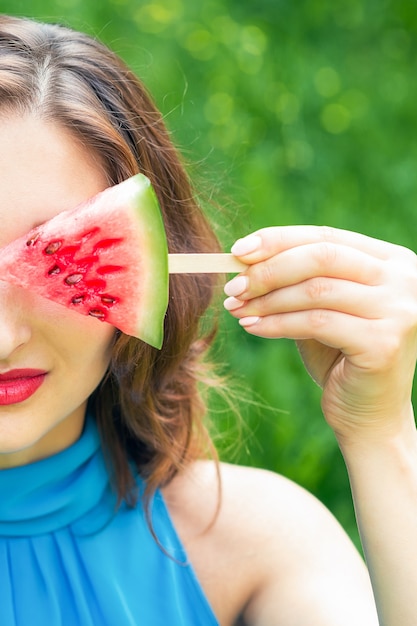 Pretty woman covers her eye with piece of watermelon.