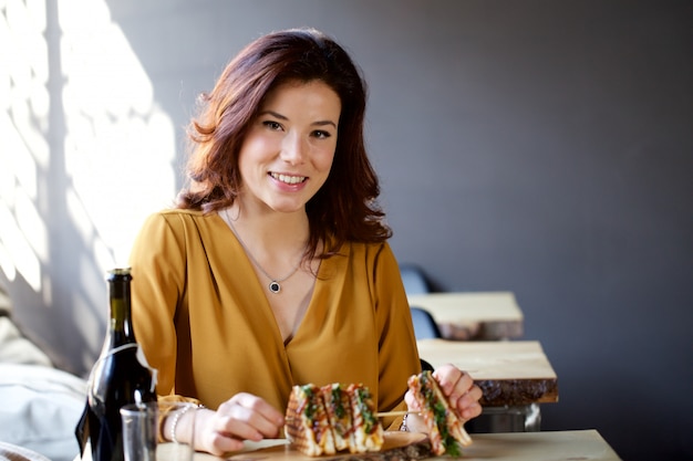 Donna graziosa che mangia un panino di club in un ristorante del pub