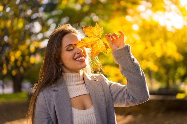 A pretty woman enjoying autumn in a park at sunset with a leaf on her face