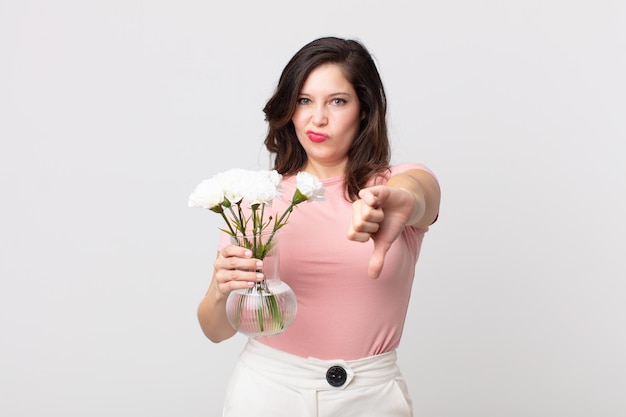 Pretty woman feeling cross,showing thumbs down and holding a decorative flowers pot