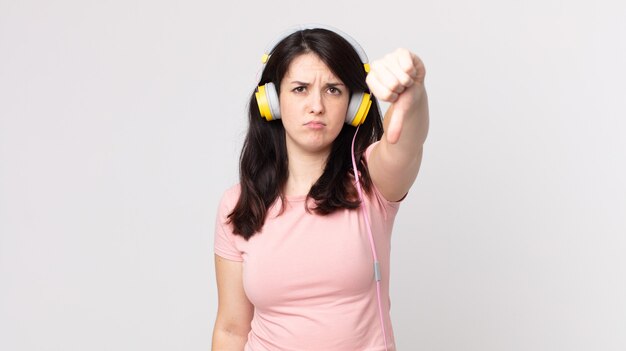 Pretty woman feeling cross,showing thumbs down listening music with headphones