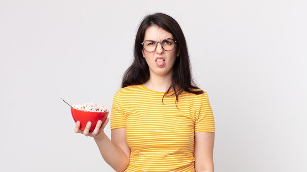 Pretty woman feeling disgusted and irritated and tongue out and holding a breakfast bowl