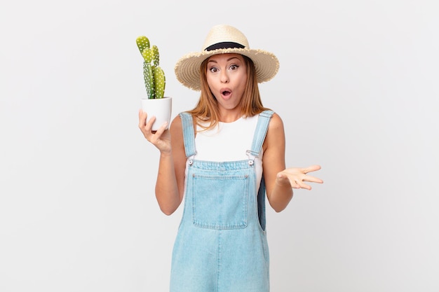 Pretty woman feeling extremely shocked and surprised and holding a cactus decorative plant